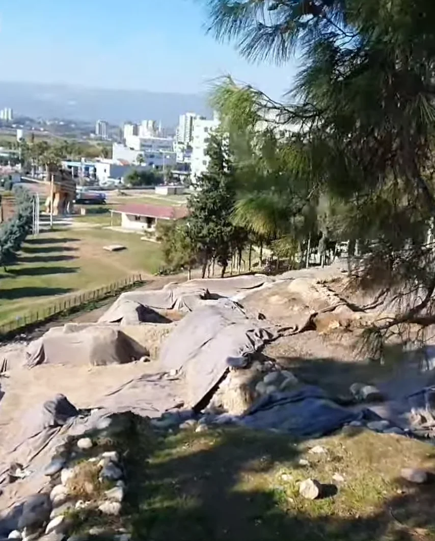 Yumuktepe'de Açık Hava Kalıntıları - Tarih ve Modernite Buluşuyor! Açık hava arkeolojik kalıntılar, modern şehir manzarası ve doğal alanlar.