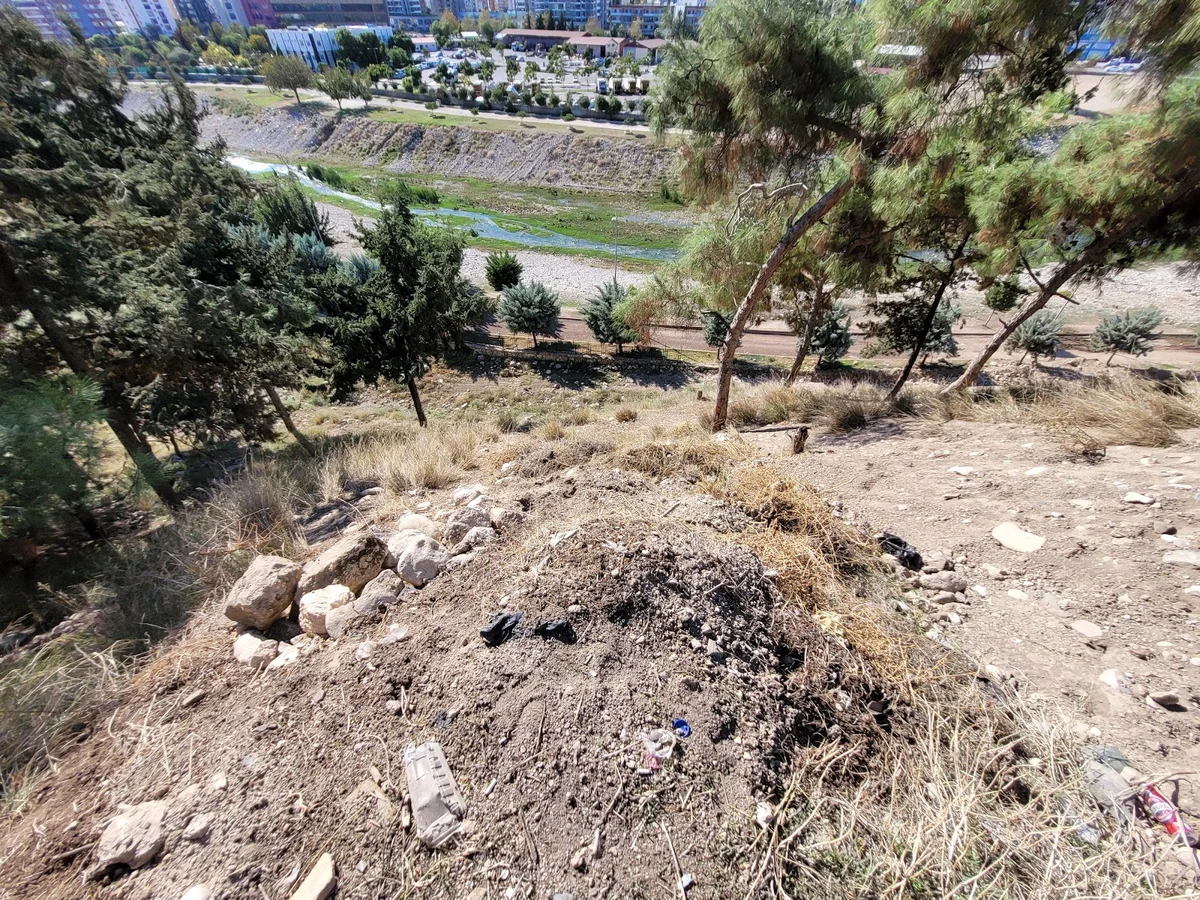 Yumuktepe'nin Doğal ve Kentsel Güzellikleri - Kuru Toprak ve Modern Binalar! Yumuktepe'den manzara; kuru toprak, taşlar, ağaçlar ve modern binalar.
