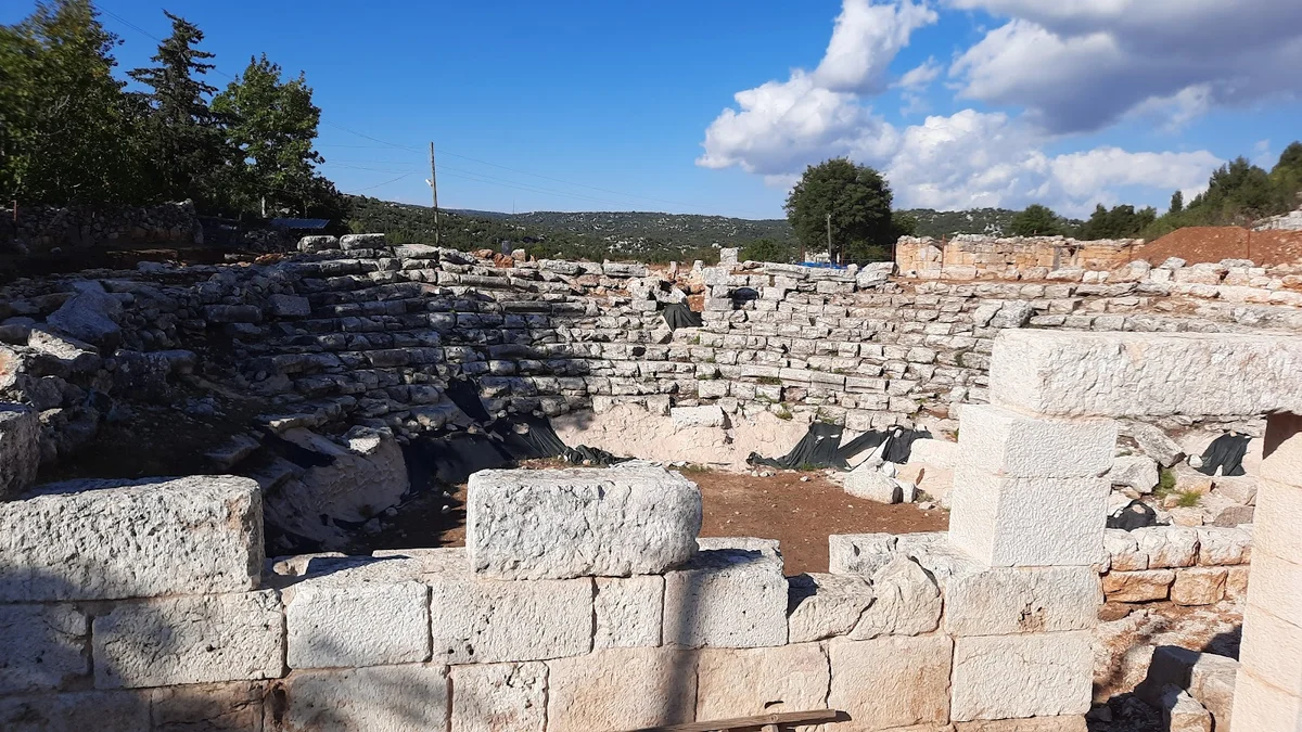 Olba Antik Kenti'nde Tarihi Tiyatro Kalıntısı - Geçmişin Sahnelerine Yolculuk! Antik tiyatro kalıntısı, taş oturma sıraları ve yeşil ağaçlarla çevrili.