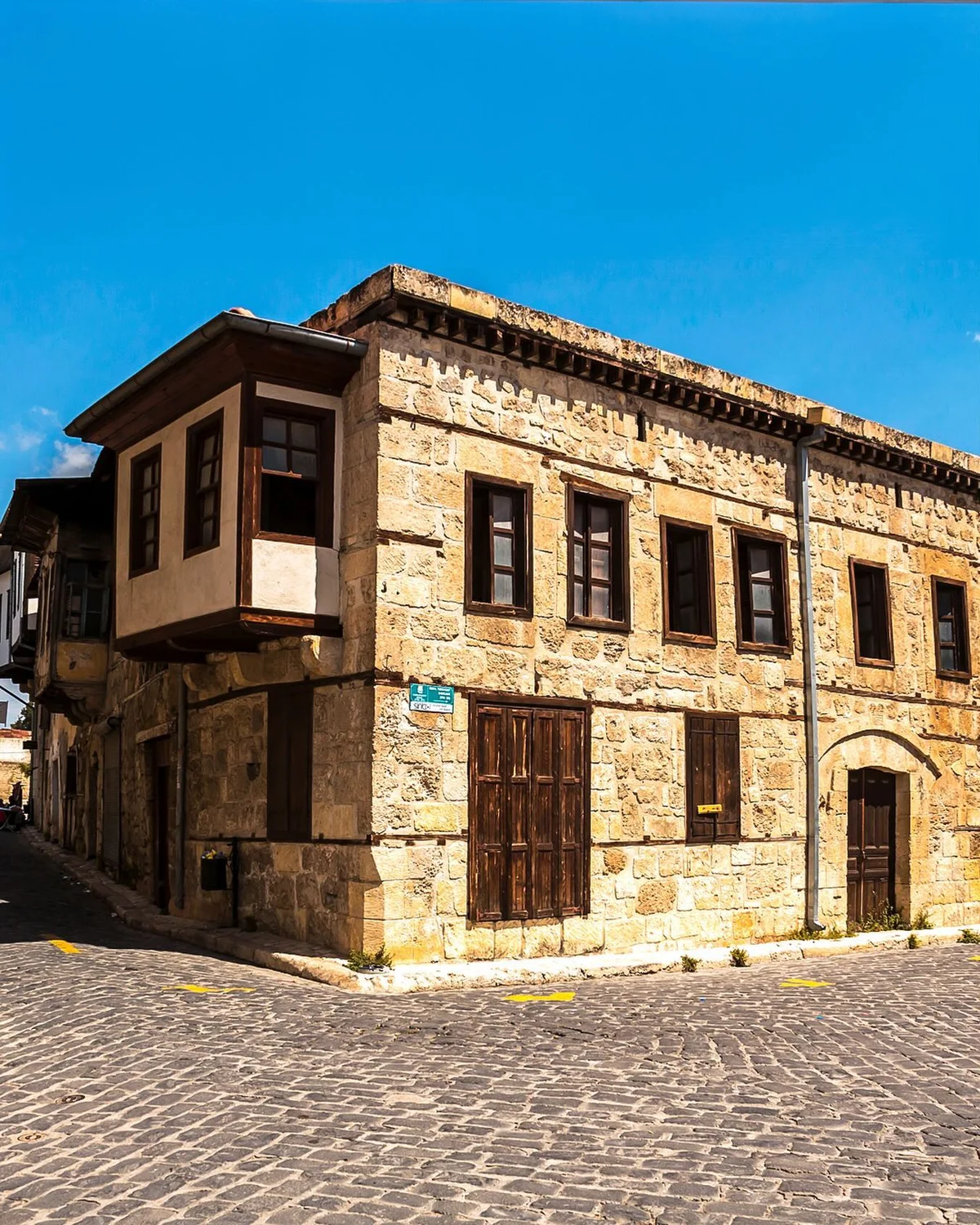 Tarsus'un Tarihi Evleri - Geçmişin İzlerinde Sanat ve Mimarlık! Neler Keşfedeceğiz? Eski taş yapıya sahip tarihi bir bina, ahşap pencereleri ve taş döşeli sokakla birlikte.