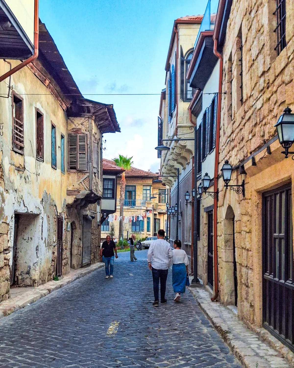 Tarihi Tarsus Evleri - Zaman Yolculuğuna Hazır mısınız? 🌍✨ Dar sokakta yürüyen insanlar, tarihi taş binalar ve palmiye ağaçları
