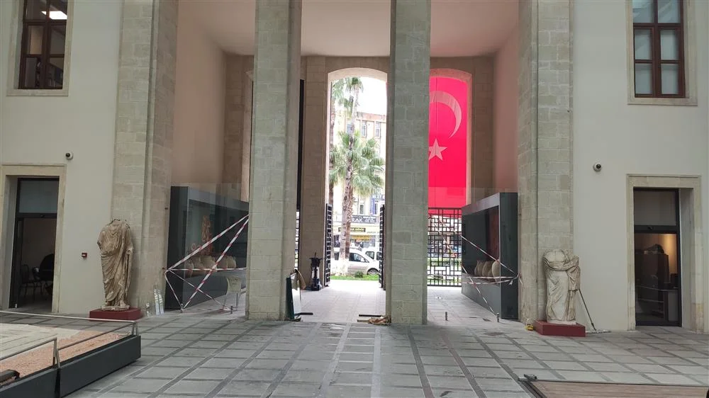 Tarsus Müzesi'nin Tarihi Atmosferi - Sütunlar ve Bayrakla Zenginleşen Alan Geniş bir alanda iki büyük sütun, taş zemin ve Türk bayrağı asılı pencere görünmekte.
