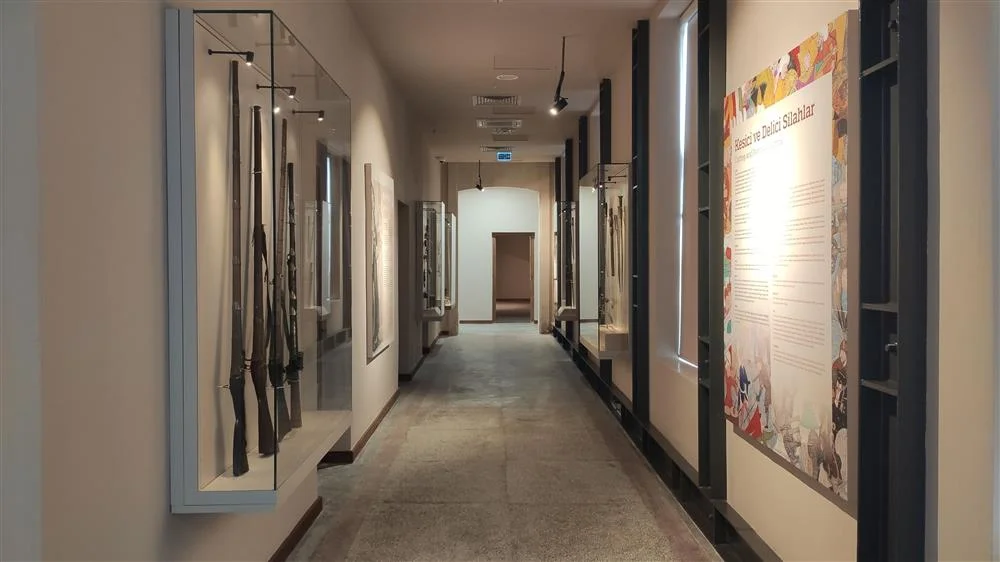 Tarsus Müzesi'nde Tarihi Silahlar Sergisi - Cam Vitrinlerde Geçmişin İzleri! Müze koridorunda cam vitrinlerde sergilenen çeşitli silahlar ve bilgi panosu