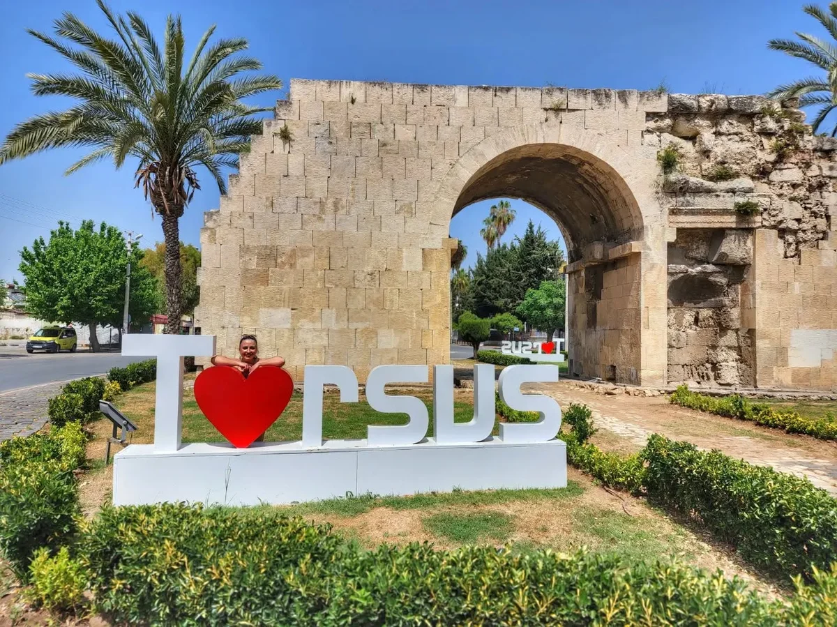 Tarsus'ta Kleopatra Kapısı ve Yaz Günü - Turistik Güzellikler! Tarsus'ta 'I ❤️ Tarsus' tabelası, arka planda tarihi yapı ve palmiye ağaçlarıyla yaz gününü yansıtıyor.