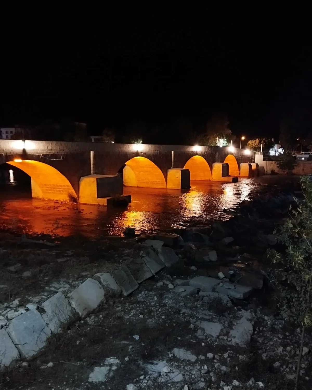 Silifke Taş Köprü Gece Manzarası - Turuncu Işıkların Dansı! Taş köprü gece ışıklarıyla aydınlatılmış, suyun altında yansıyan turuncu ışıklar göz alıyor.
