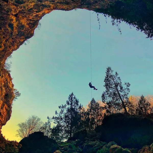 Kocain Mağarası'nda ip ile inen bir dağcı, sarı ve turuncu taşlarla aydınlatılmış tavanı gösteriyor.