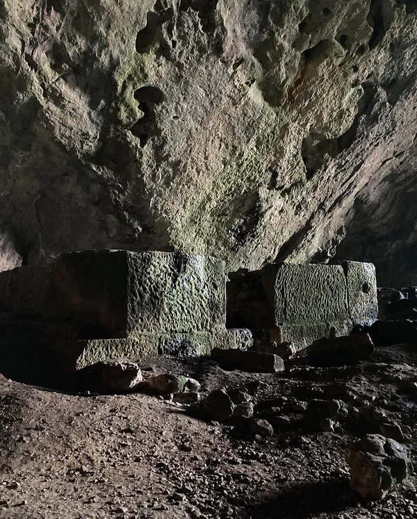 Büyük bir mağara içi, kayalık duvarlar ve taş bloklarla dolu karanlık atmosfer