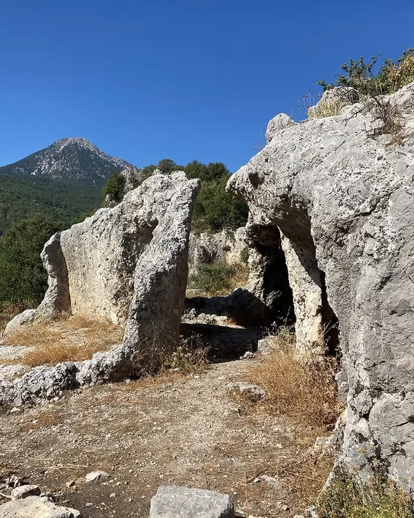 Açık mavi gökyüzü altında büyük taş kalıntıları ve yeşil orman