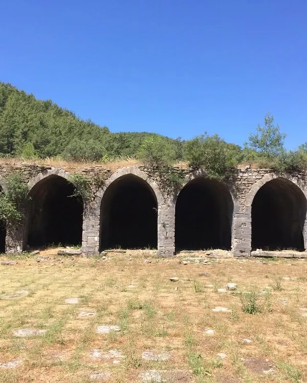 Antik taş duvarlarla çevrili, yeşil doğa içinde büyük kemerli yapı