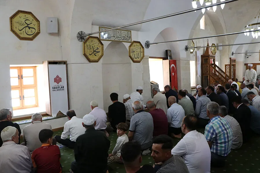 Cami içinde dua eden kalabalık bir topluluk, yüksek kubbeler ve Arap harfleriyle yazılmış ayetler