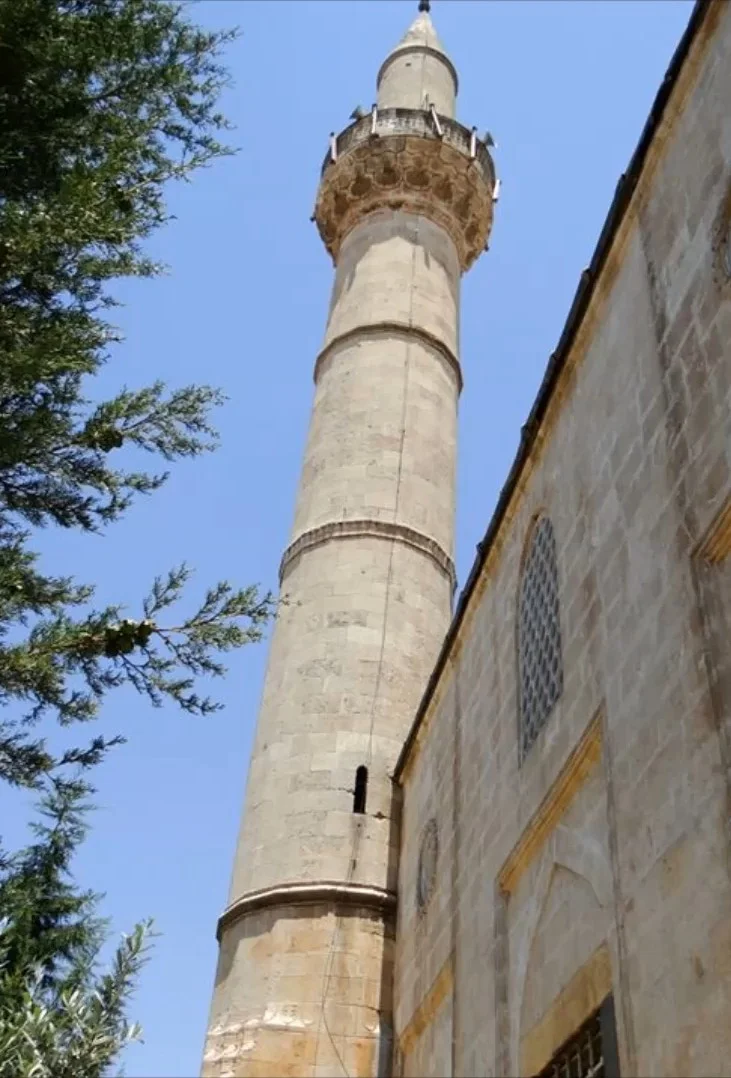 Güneşli günde Canbolat Paşa Camii'nin yüksek minaresi ve çevresindeki yeşil ağaçlar