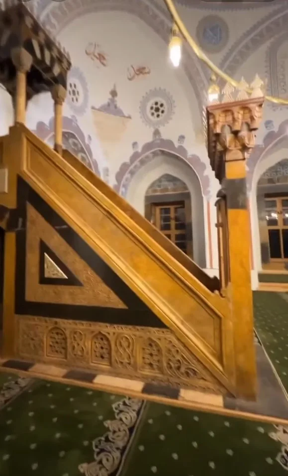 Ahşap minber detaylı oymalarla süslenmiş, arka planda zarif pencereler var.