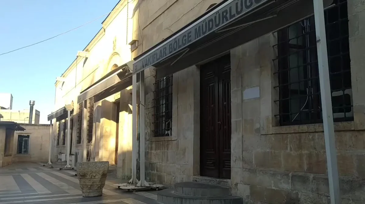 Taş yapı, sarı tonları, demir parmaklıklı pencereler ve vakıf tabelasıyla Cüneyne Camii'nin cephesi.