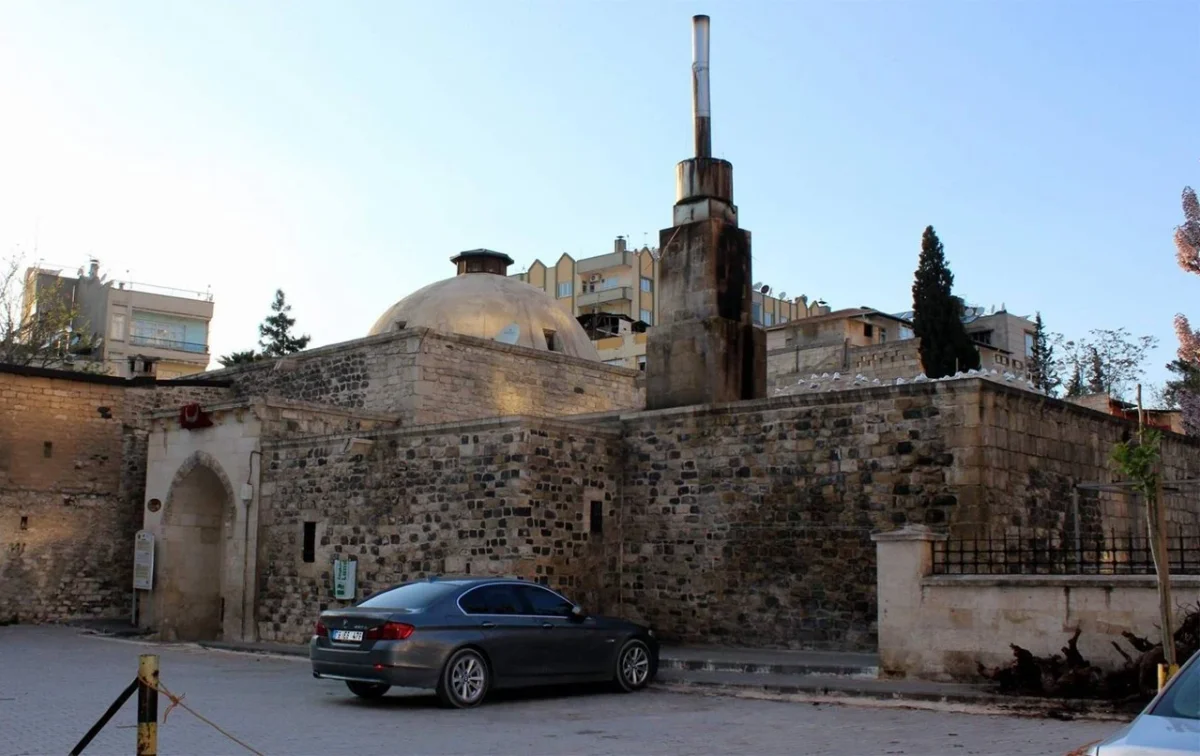 Tarihi taş yapı, yuvarlak kubbe ve modern apartmanlarla çevrili.